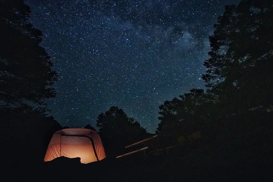 A glowing tent rests beneath a sky full of stars.