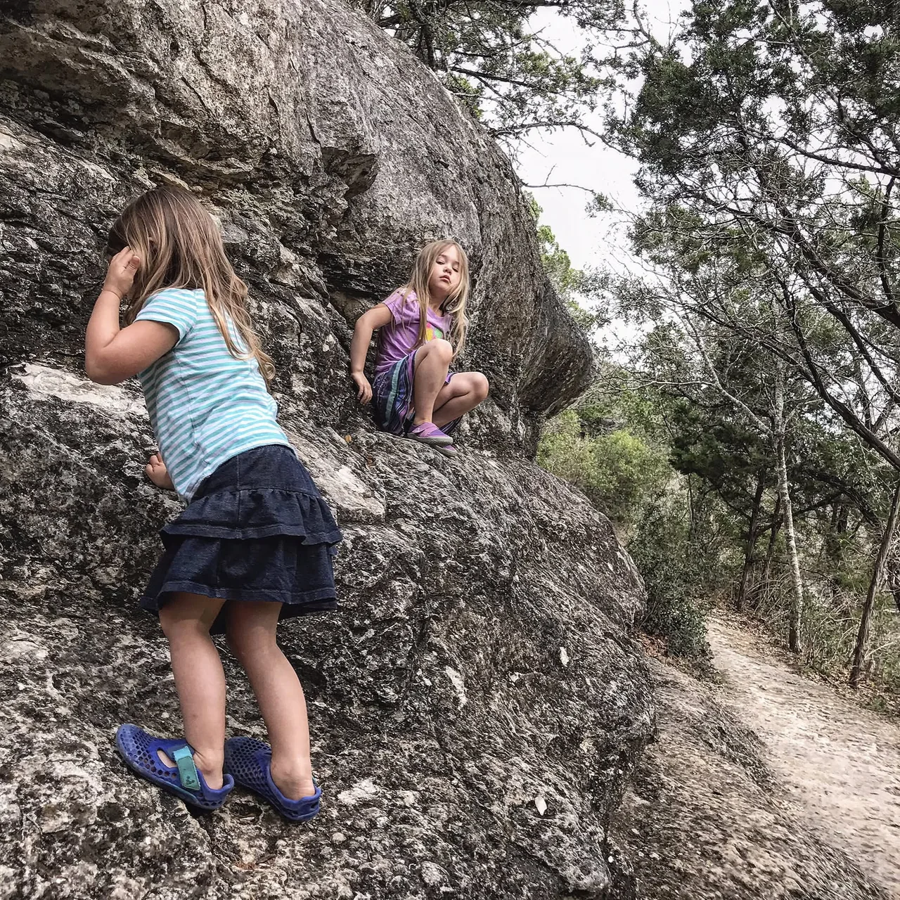 Children climb among large boulders in the woods.