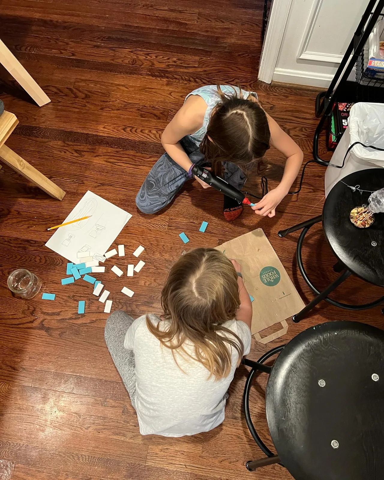 The girls assemble a bird feeder on the floor.