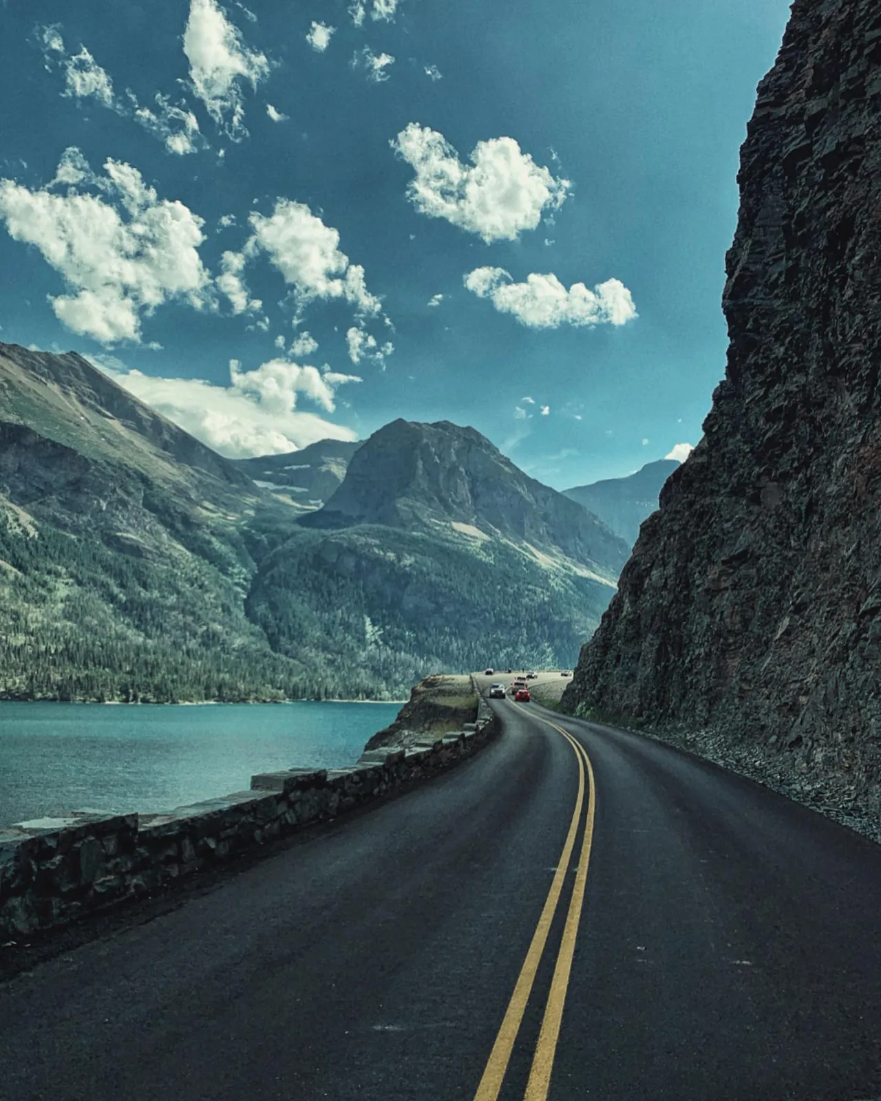 A road curves beside a turquoise lake and steep mountain walls.