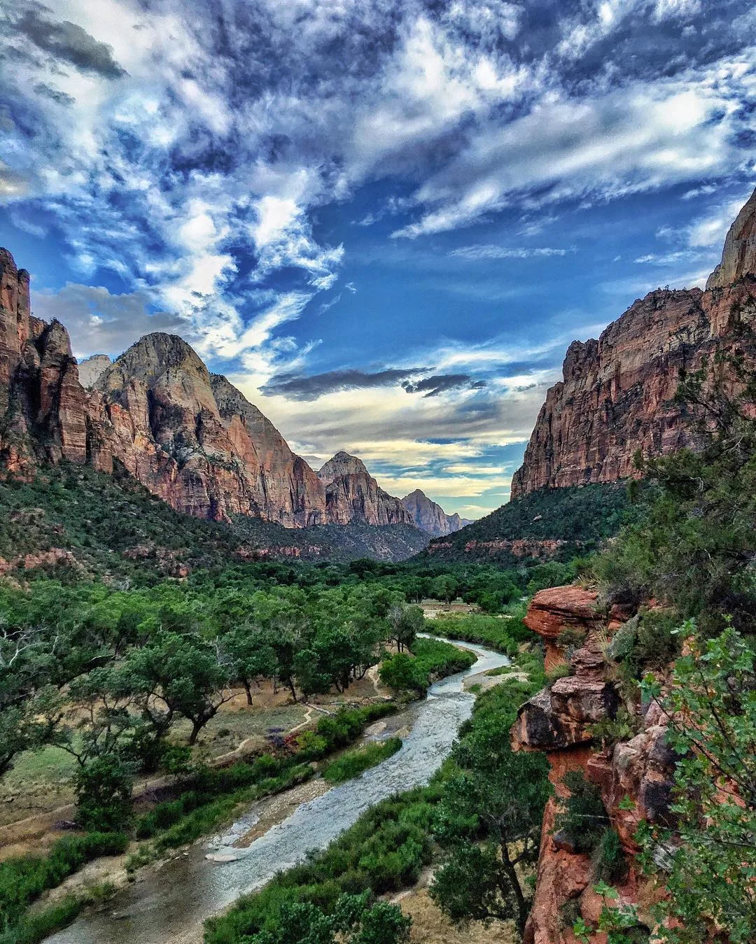 A green river valley winds between red sandstone cliffs.
