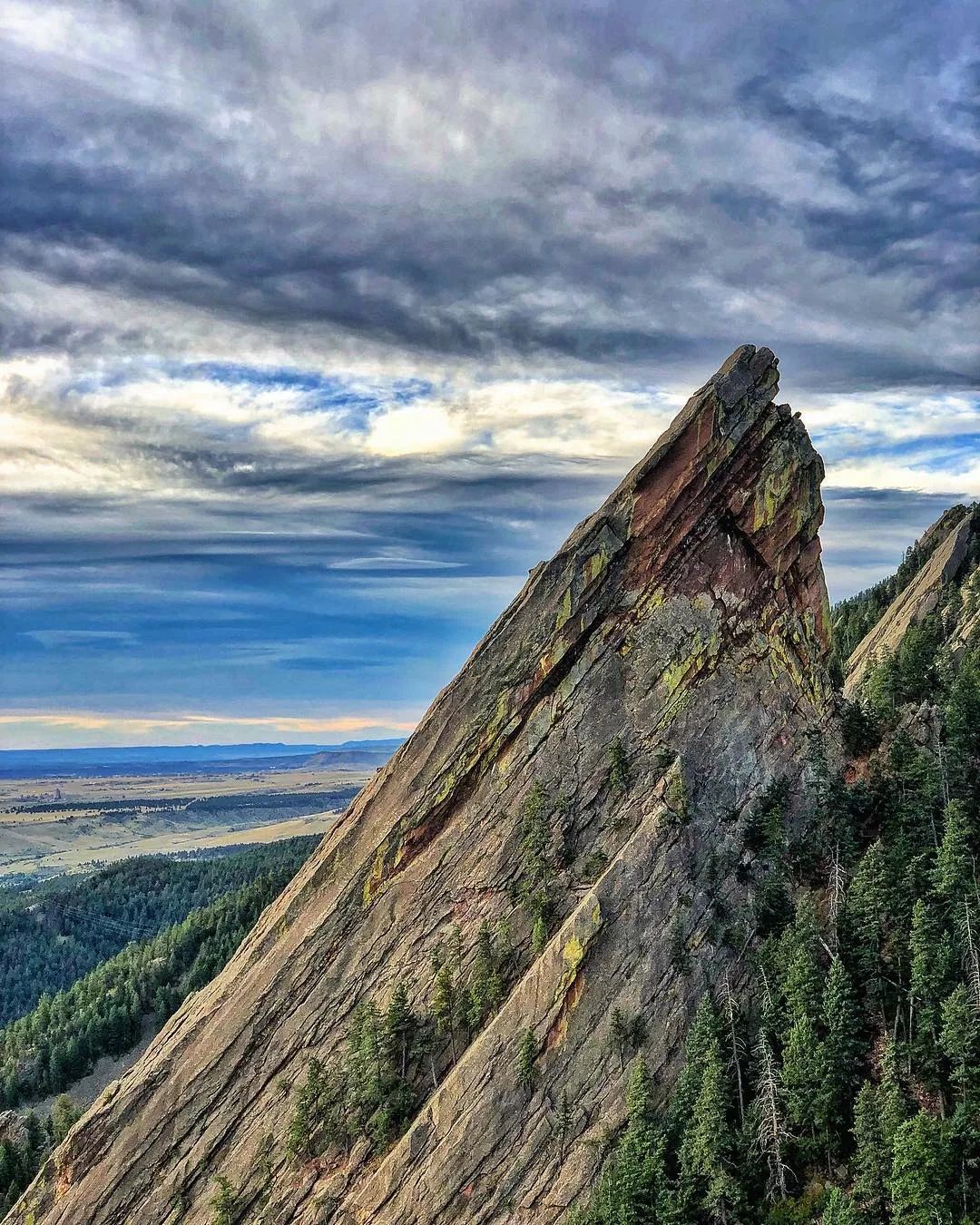 A steep rock formation points toward a blue, cloud-filled sky.