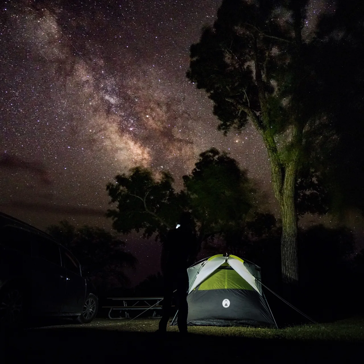 The Milky Way rises over a campsite and a glowing tent.